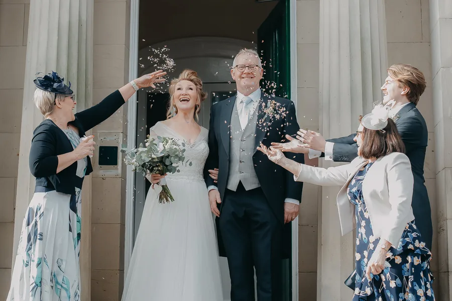 Brudpar med gäster som kastar konfetti under ett firande fotograferat av Alnwick Photo